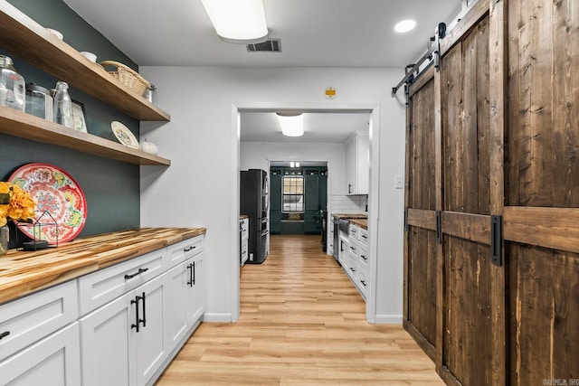 kitchen featuring a barn door, visible vents, white cabinets, butcher block counters, and freestanding refrigerator