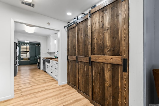 kitchen featuring a barn door, visible vents, white cabinets, light wood-style flooring, and freestanding refrigerator