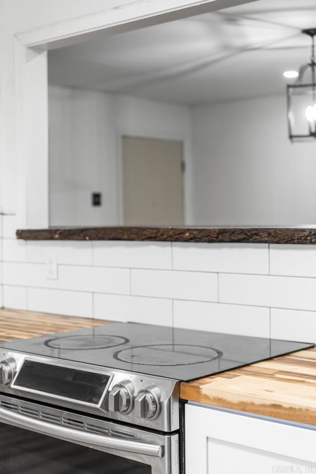 kitchen featuring stainless steel electric range oven, butcher block counters, backsplash, and white cabinets