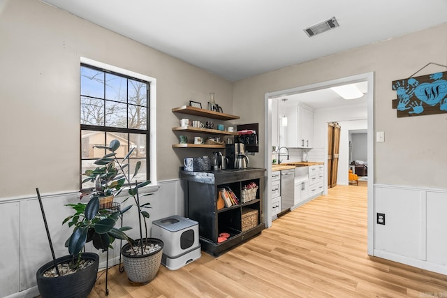 office space featuring light wood-type flooring, visible vents, a sink, and wainscoting