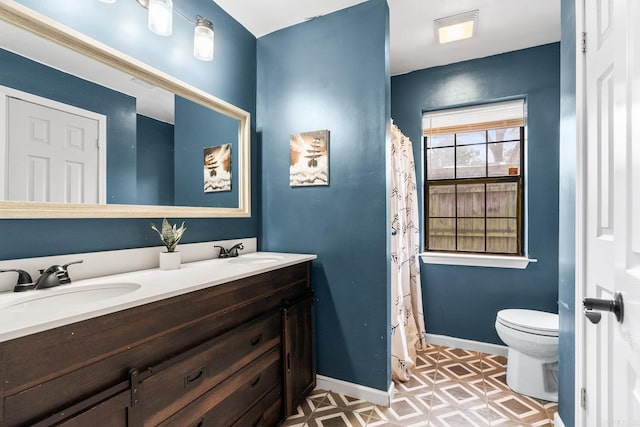 full bath featuring toilet, a sink, baseboards, and double vanity