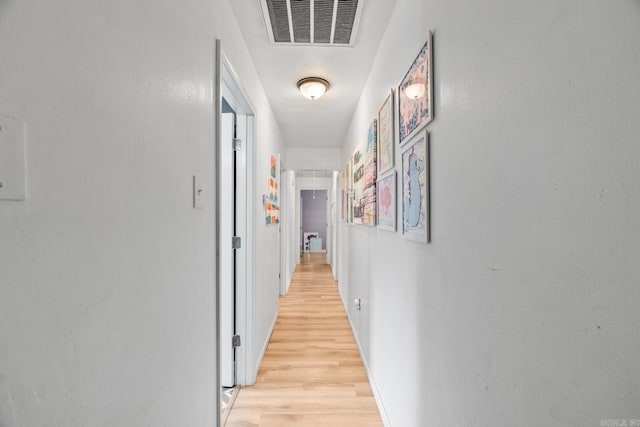 hallway with light wood finished floors, baseboards, and visible vents