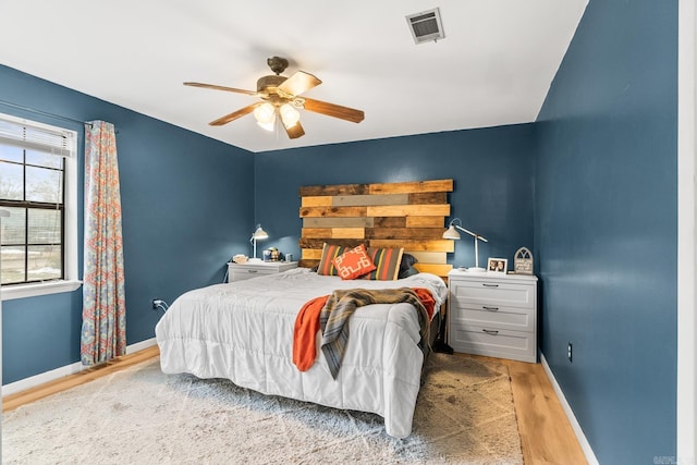 bedroom featuring a ceiling fan, visible vents, baseboards, and wood finished floors