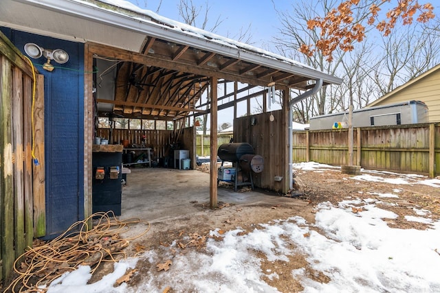 snow covered patio featuring fence, area for grilling, and an outdoor structure