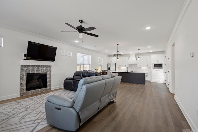 living area with dark wood-style floors, baseboards, crown molding, and a tiled fireplace