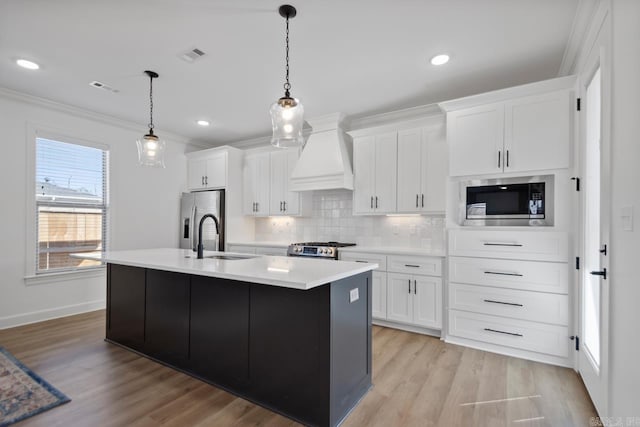 kitchen with a center island with sink, visible vents, appliances with stainless steel finishes, premium range hood, and a sink