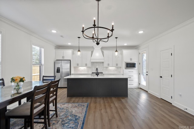 kitchen featuring crown molding, a center island with sink, built in microwave, and stainless steel fridge with ice dispenser