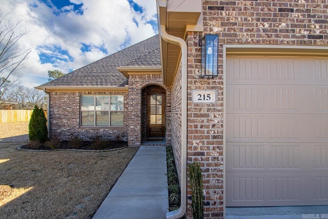 doorway to property featuring a garage, brick siding, and roof with shingles