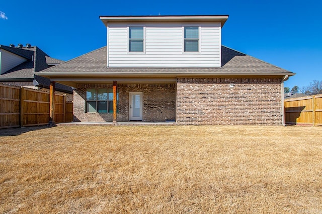 back of property with roof with shingles, fence, a lawn, and brick siding