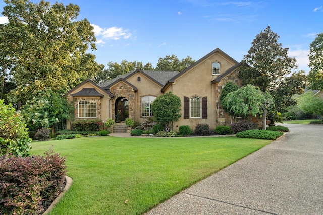 french provincial home featuring stone siding, stucco siding, and a front yard