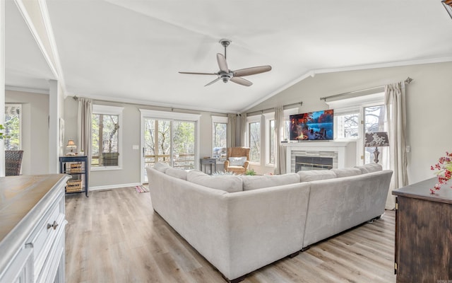 living area with light wood finished floors, ornamental molding, a glass covered fireplace, vaulted ceiling, and ceiling fan