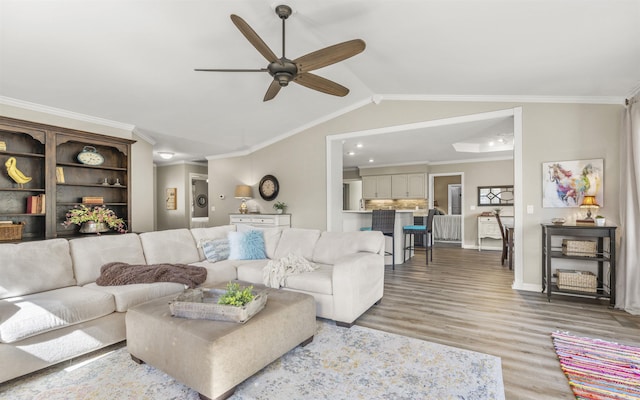 living room with baseboards, a ceiling fan, light wood-style flooring, vaulted ceiling, and crown molding