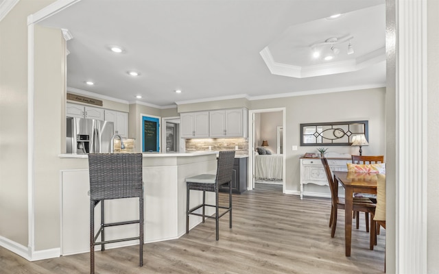 kitchen featuring a peninsula, light wood-type flooring, stainless steel fridge, and a kitchen bar