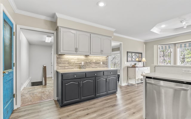 kitchen featuring light countertops, stainless steel dishwasher, light wood-type flooring, tasteful backsplash, and crown molding