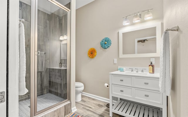 bathroom featuring toilet, wood finished floors, vanity, baseboards, and a stall shower