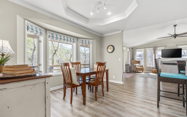 dining room with light wood finished floors, baseboards, a raised ceiling, a ceiling fan, and crown molding