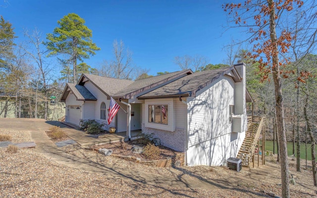 view of front of house featuring an attached garage, brick siding, stairs, driveway, and a chimney