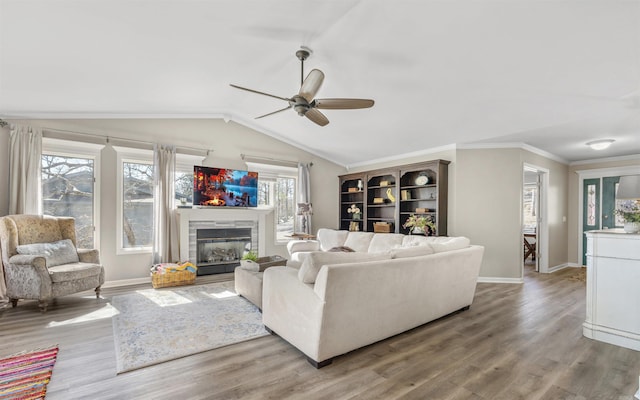 living room with vaulted ceiling, ornamental molding, a glass covered fireplace, and light wood-style flooring