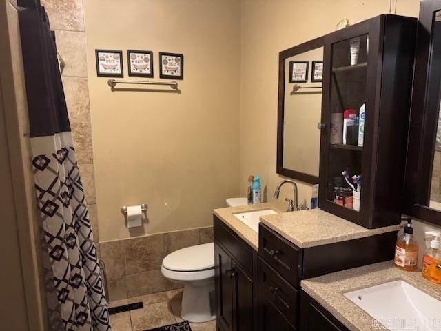 bathroom with a shower with shower curtain, vanity, toilet, and tile patterned floors