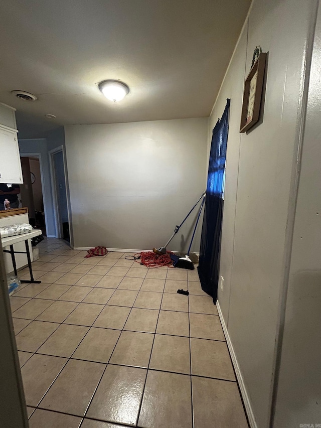 hallway with visible vents, baseboards, and light tile patterned floors