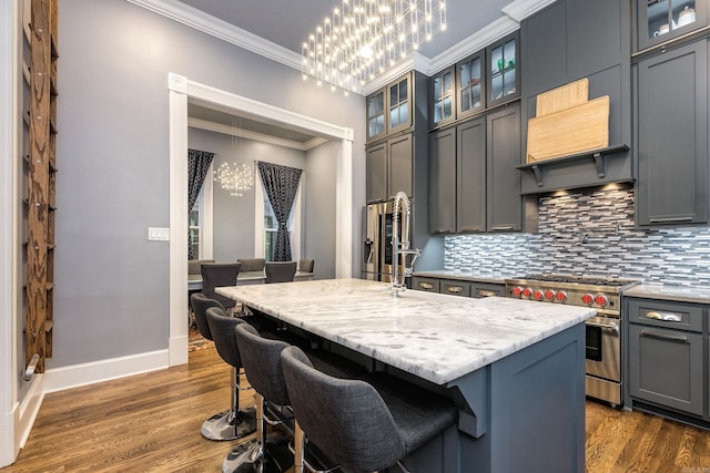 kitchen featuring crown molding, decorative backsplash, dark wood-type flooring, an island with sink, and double oven range