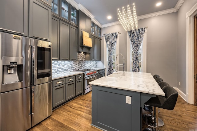 kitchen with stainless steel appliances, wood finished floors, a sink, ornamental molding, and backsplash