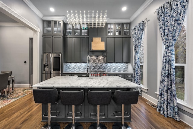 kitchen featuring crown molding, stainless steel refrigerator with ice dispenser, visible vents, backsplash, and a kitchen island with sink