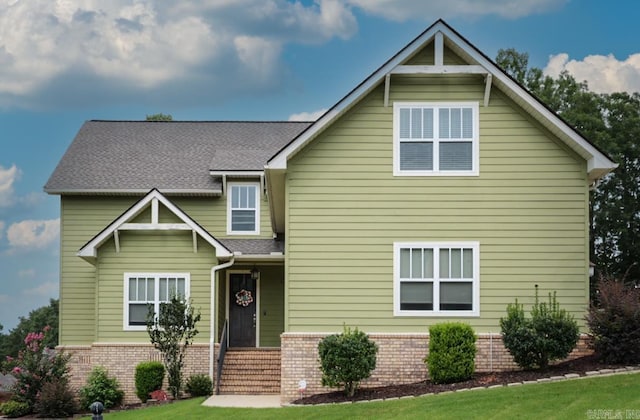 craftsman house featuring roof with shingles, a front lawn, and brick siding