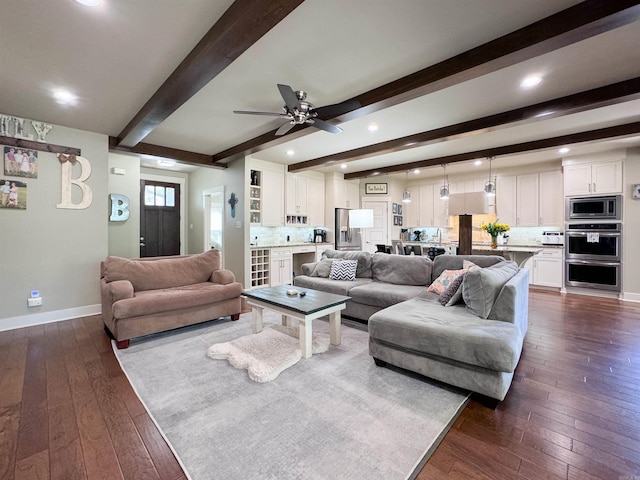 living area featuring a ceiling fan, beam ceiling, dark wood finished floors, and baseboards