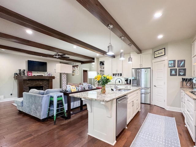 kitchen with light stone counters, dark wood finished floors, stainless steel appliances, white cabinetry, and a sink