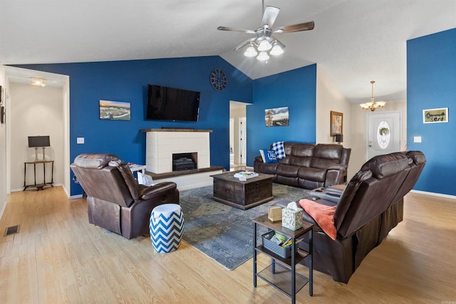 living room with a fireplace with raised hearth, ceiling fan with notable chandelier, wood finished floors, visible vents, and vaulted ceiling