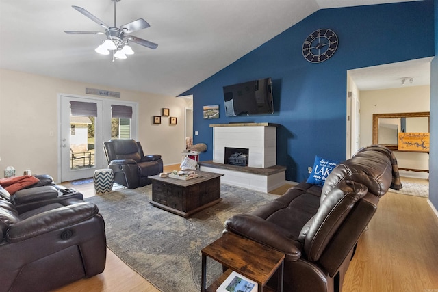 living room with lofted ceiling, ceiling fan, a fireplace with raised hearth, and wood finished floors