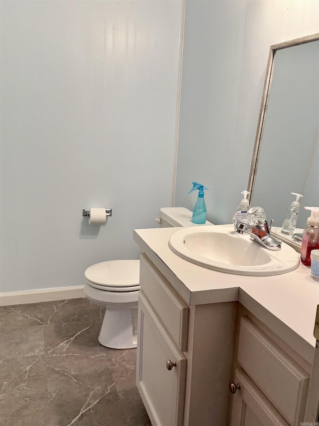 half bathroom featuring toilet, marble finish floor, vanity, and baseboards