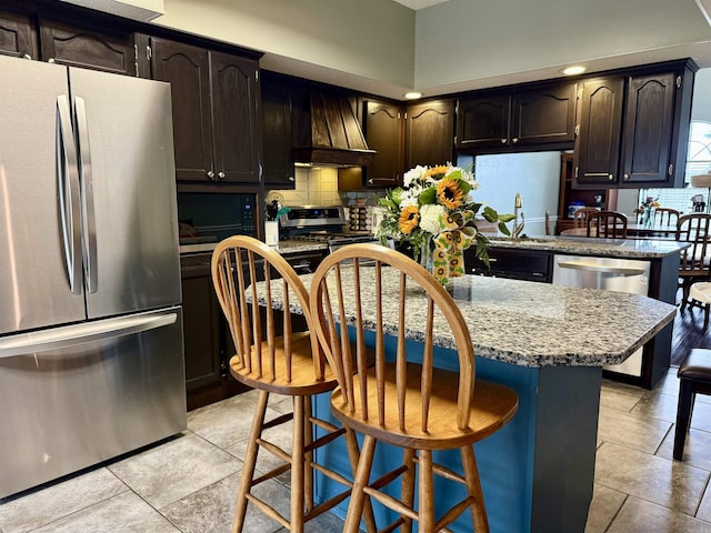 kitchen featuring a breakfast bar, custom exhaust hood, backsplash, appliances with stainless steel finishes, and a sink