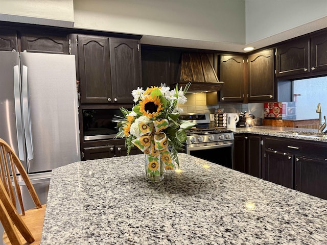 kitchen with stainless steel appliances, custom range hood, a sink, and light stone countertops