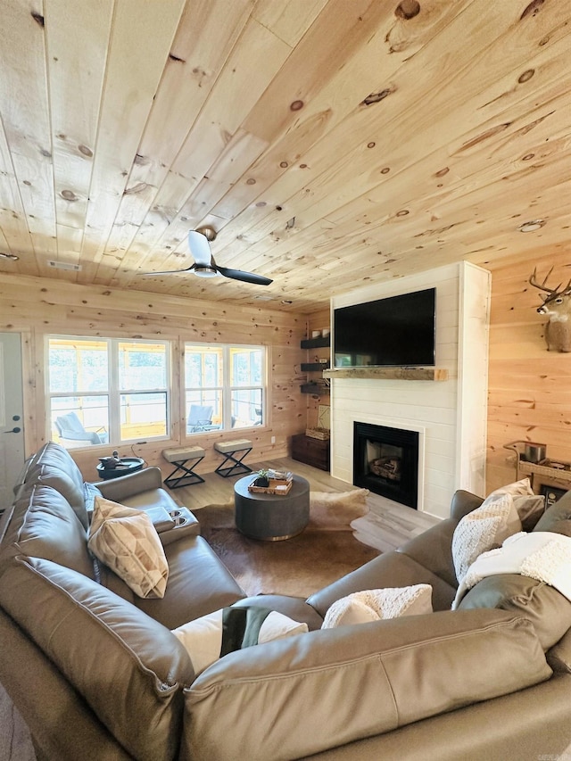 living area featuring wooden ceiling, wood walls, a fireplace with raised hearth, and wood finished floors