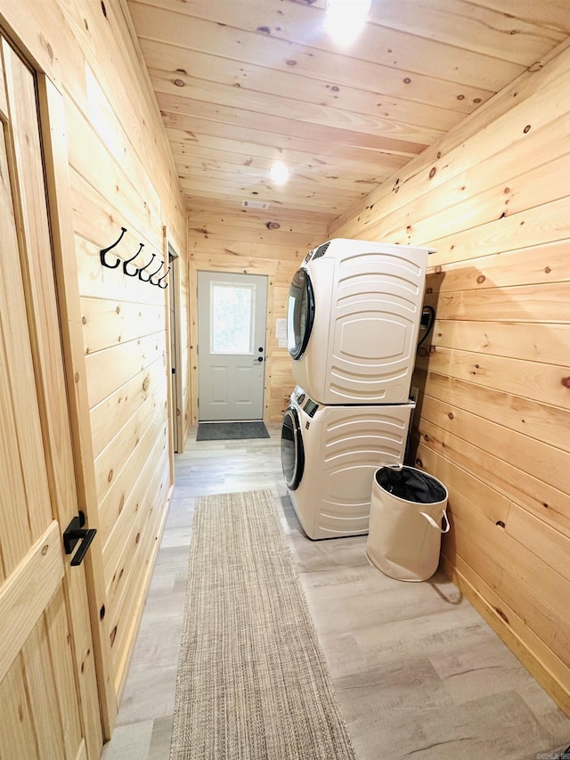 laundry area featuring laundry area, light wood-style floors, wooden ceiling, wood walls, and stacked washing maching and dryer