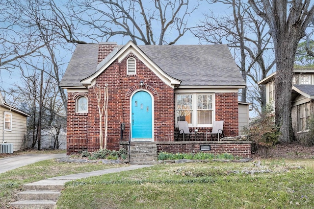 view of front of home with brick siding, roof with shingles, and a front lawn