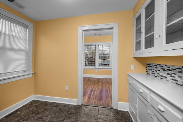 interior space featuring tasteful backsplash, light countertops, visible vents, and glass insert cabinets