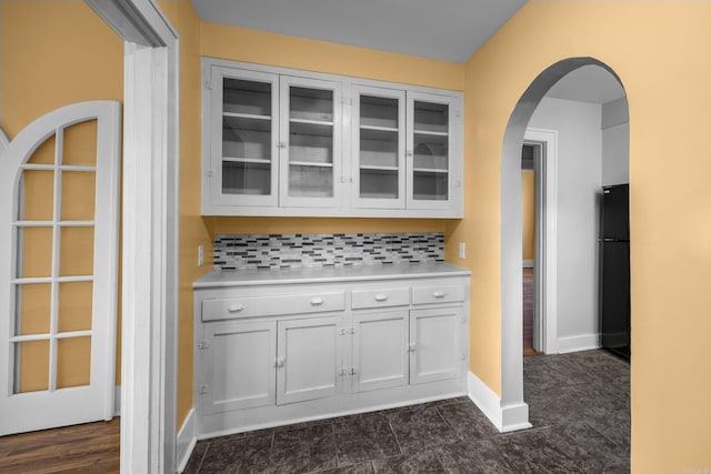 interior space featuring tasteful backsplash, freestanding refrigerator, arched walkways, and baseboards