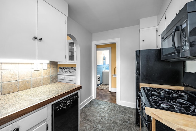 kitchen with baseboards, white cabinets, decorative backsplash, black appliances, and stone finish floor