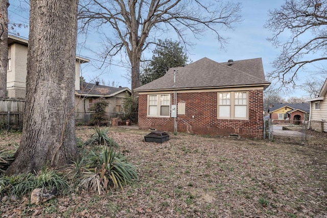 rear view of house with roof with shingles, fence, and brick siding