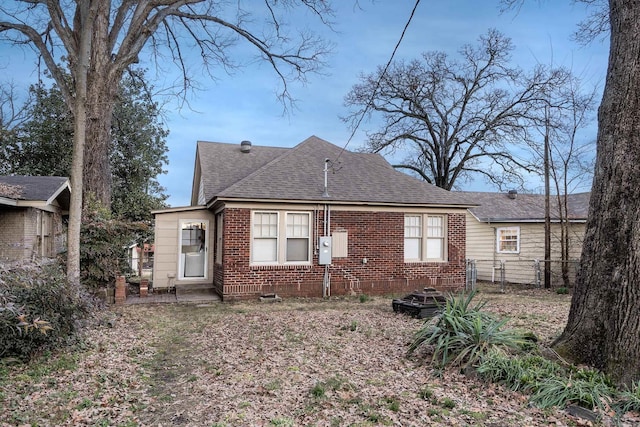 rear view of property featuring brick siding, a shingled roof, and fence