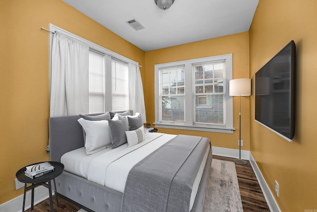 bedroom with baseboards, visible vents, and wood finished floors