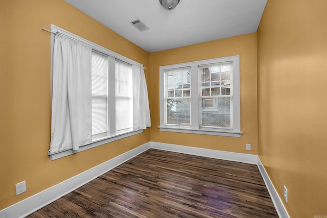 unfurnished room featuring dark wood finished floors, visible vents, and baseboards