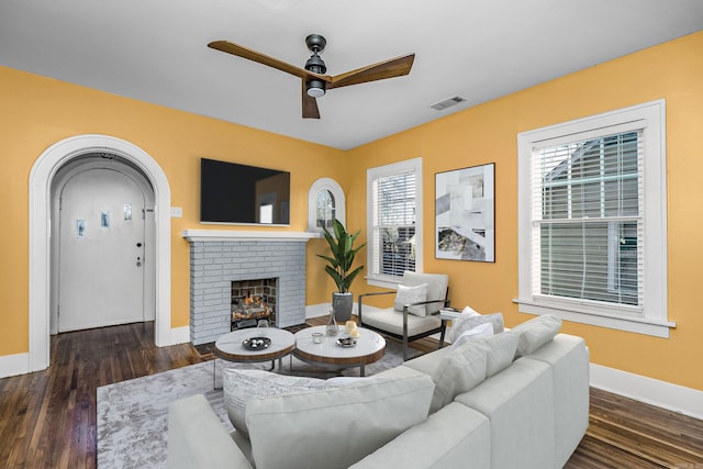 living area featuring a brick fireplace, ceiling fan, visible vents, and wood finished floors