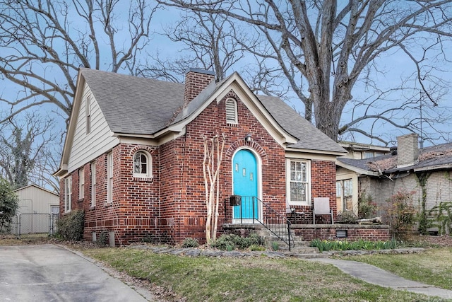 view of front facade with brick siding, a chimney, and roof with shingles