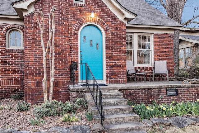 property entrance featuring brick siding and a shingled roof