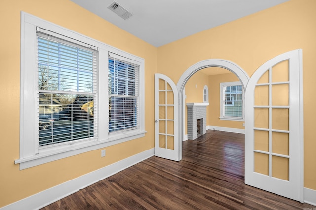 unfurnished room with a wealth of natural light, visible vents, baseboards, and wood finished floors