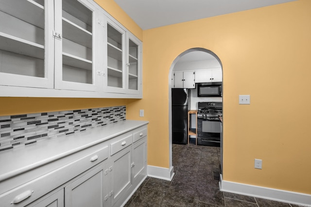 kitchen with arched walkways, light countertops, backsplash, black appliances, and glass insert cabinets